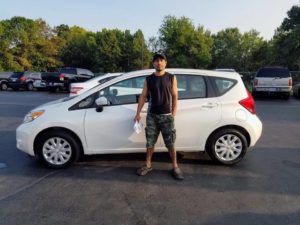 Green Light Auto Customer in front of White Nissan Versa